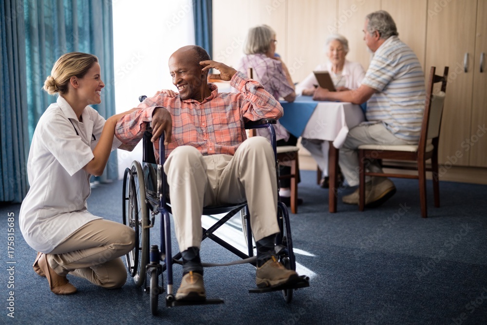 Smiling female doctor kneeling by disabled senior man sitting on Smiling female doctor kneeling by disabled senior man sitting on