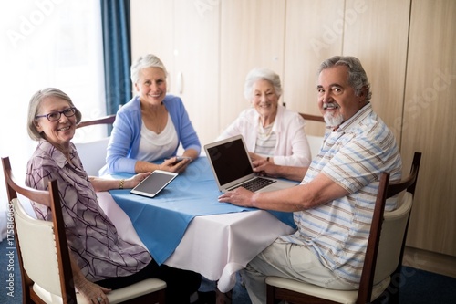 Smiling seniors sitting with technologies at table