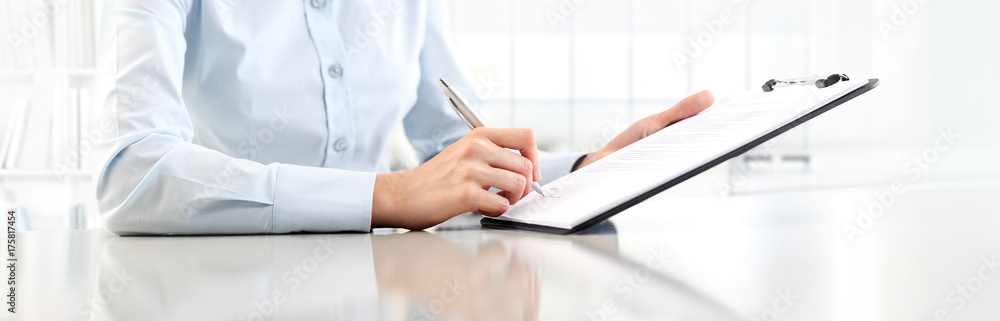 Woman's hands writing on sheet in a clipboard with a pen, isolated on desk Woman's hands writing on sheet in a clipboard with a pen, isolated on desk