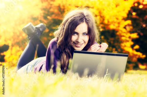 Young woman using laptop in the park lying on the green grass