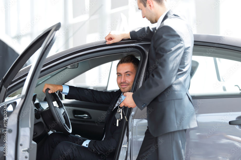 successful businessman, receiving the keys to the car from the seller in the showroom