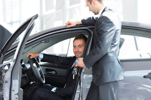 successful businessman, receiving the keys to the car from the seller in the showroom © ASDF