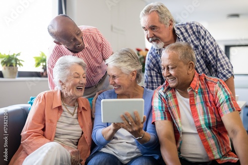 Senior woman showing digital tablet to cheerful friends