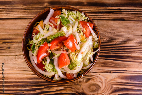 Dietary salad with the chinese cabbage and tomatoes in ceramic bowl on a wooden table. Top view