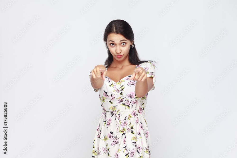 Hey you! Young adult woman, pointing finger and looking at camera. On gray background. Indoor, studio shot Hey you! Young adult woman, pointing finger and looking at camera. On gray background. Indoor, studio shot