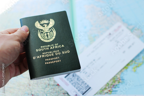A South African passport in a man's hand with a plane ticket and map in the background. This image can be used to represent emigration or travelling. This image has selective focusing. 