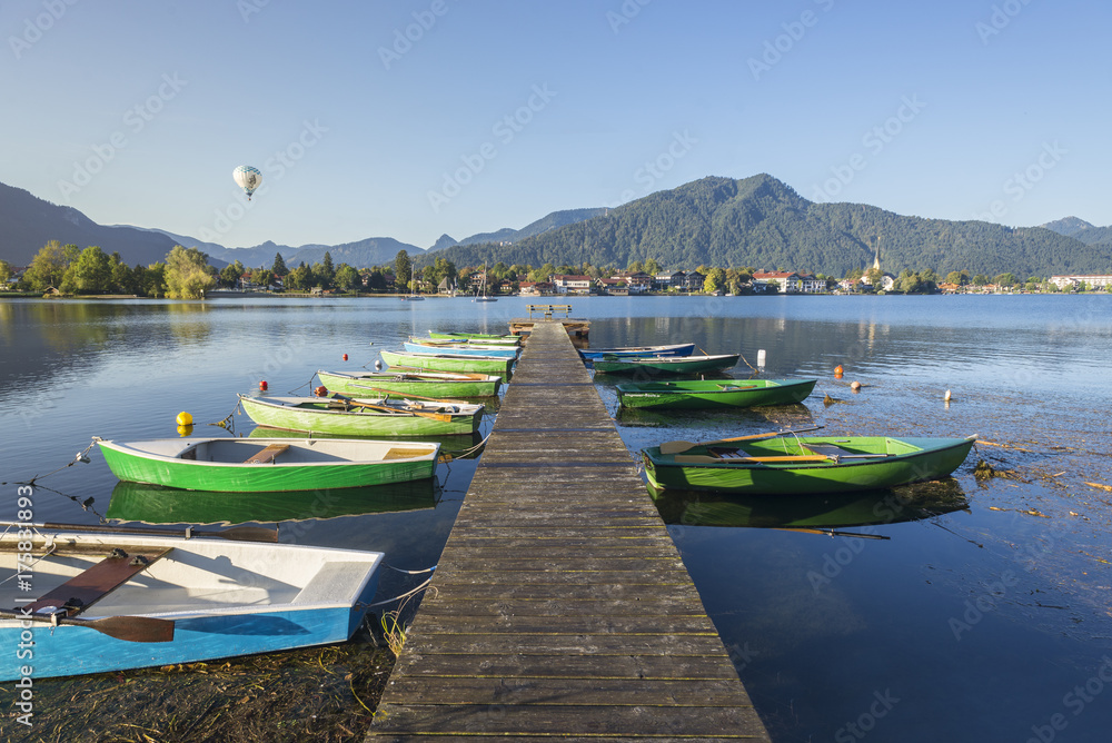Ruderboote an einem Holzsteg im Tegernsee mit Blick auf Rottach-Egern und Ballonfahrer in der Morgensone Ruderboote an einem Holzsteg im Tegernsee mit Blick auf Rottach-Egern und Ballonfahrer in der Morgensone