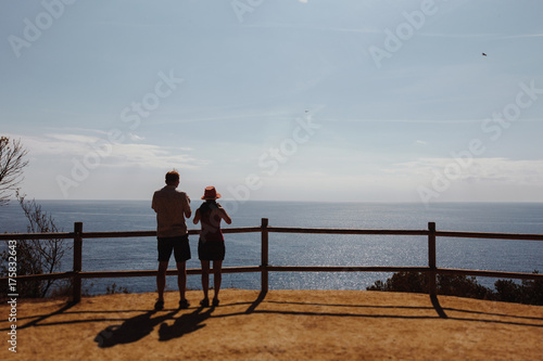 two tourists a guy and a girl stand with their backs facing the sea from a great height. Make a photo for memory. Spain