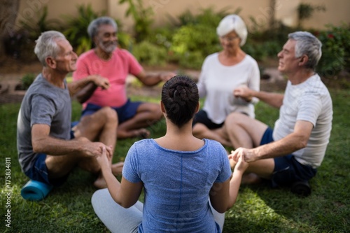 Trainer holding hands and meditating with senior men and women 