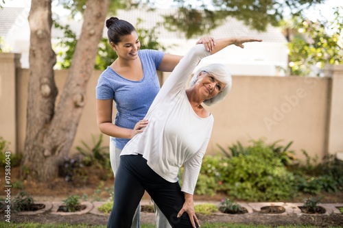 Smiling trainer assisting senior woman with hand raised