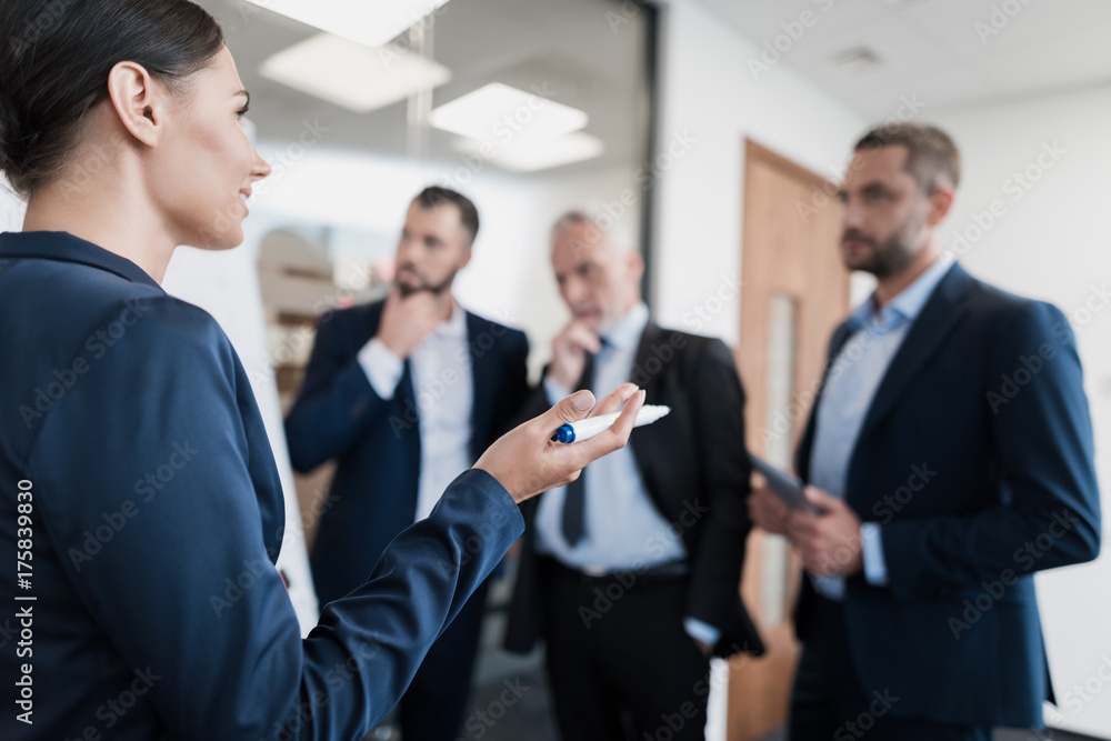 Three employees and their director are next to the rack with the schedule. They carefully consider it Three employees and their director are next to the rack with the schedule. They carefully consider it