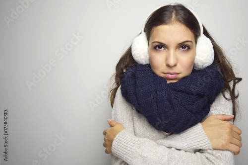 Shivering young woman being cold wearing earmuffs, sweater and scarf. Copy space.