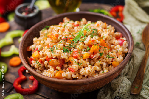 Billede på lærred Vegetarian crumbly pearl barley porridge with vegetables  in a dark background