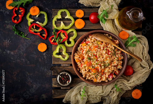 Vegetarian crumbly pearl barley porridge with vegetables in a dark background. Flat lay. Top view
