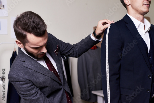 Portrait of modern tailor measuring arm length of bespoke suit during model fitting in traditional atelier studio photo