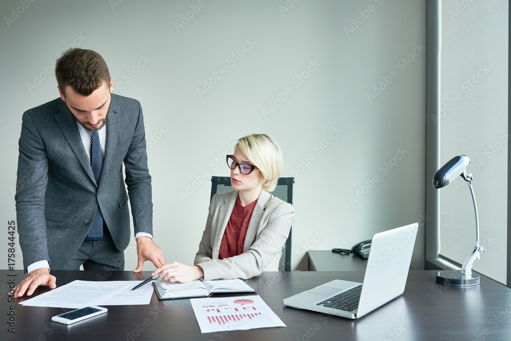 Portrait of two successful business people working at desk in modern office reading financial documents and analyzing marketing statistics Portrait of two successful business people working at desk in modern office reading financial documents and analyzing marketing statistics