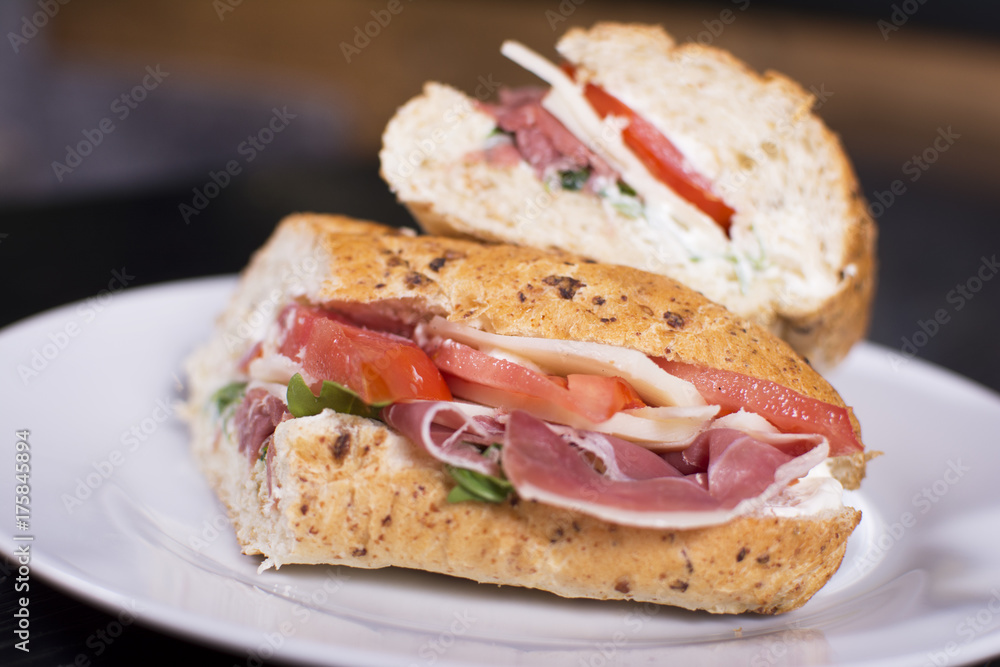 Fresh sandwich with ham, cheese, bacon, tomatoes, lettuce, cucumbers and onions on dark wooden background. Delicious restaurant meal. Fresh sandwich with ham, cheese, bacon, tomatoes, lettuce, cucumbers and onions on dark wooden background. Delicious restaurant meal.