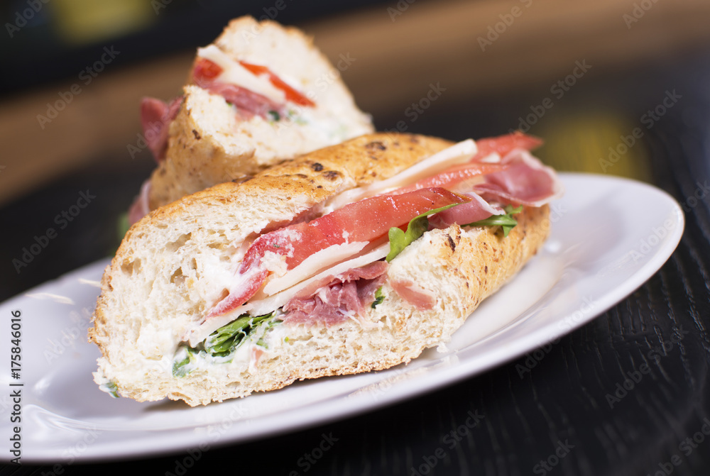 Fresh sandwich with ham, cheese, bacon, tomatoes, lettuce, cucumbers and onions on dark wooden background. Delicious restaurant meal. Fresh sandwich with ham, cheese, bacon, tomatoes, lettuce, cucumbers and onions on dark wooden background. Delicious restaurant meal.