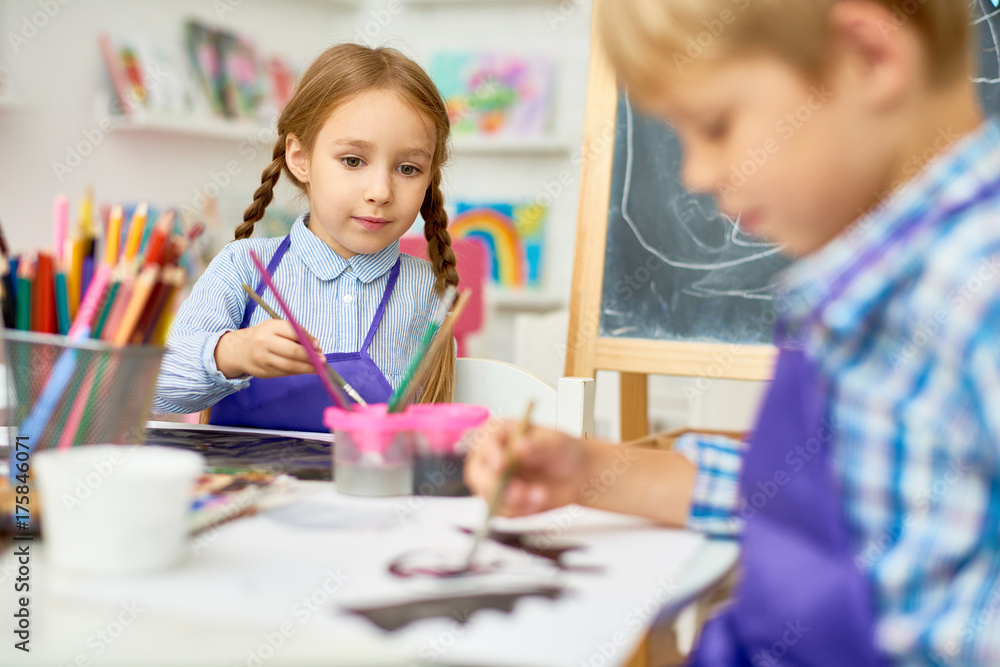 Portrait of adorable little girl painting pictures enjoying art class in pre school working together with boy Portrait of adorable little girl painting pictures enjoying art class in pre school working together with boy