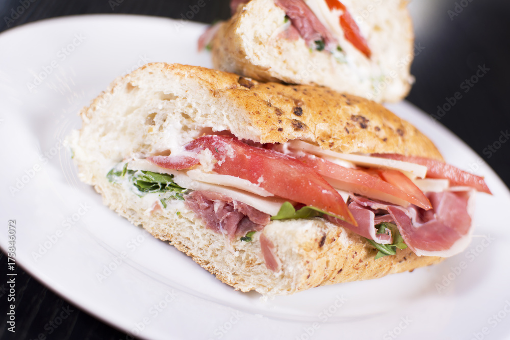 Fresh sandwich with ham, cheese, bacon, tomatoes, lettuce, cucumbers and onions on dark wooden background. Delicious restaurant meal. Fresh sandwich with ham, cheese, bacon, tomatoes, lettuce, cucumbers and onions on dark wooden background. Delicious restaurant meal.