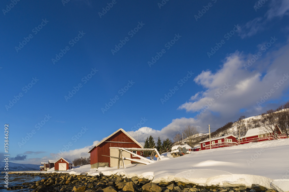 Typical norwegian warm and cozy house located at the lakeside at a fjord in a snowy winter landscape.