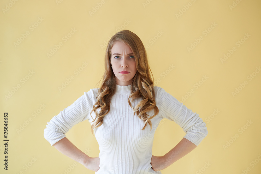 Picture of irritated young Caucasian woman in roll-neck sweater standing at yellow studio wall with hands on her waist, frowning, her posture and look expressing anger or annoyance. Body language Picture of irritated young Caucasian woman in roll-neck sweater standing at yellow studio wall with hands on her waist, frowning, her posture and look expressing anger or annoyance. Body language
