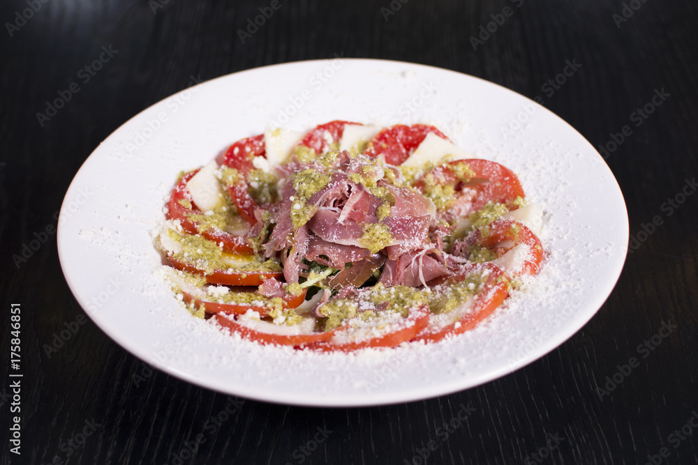Delicious salad, prosciutto, and mozzarella cheese over dark background. Close up view of a delicious restaurant meal. Delicious salad, prosciutto, and mozzarella cheese over dark background. Close up view of a delicious restaurant meal.