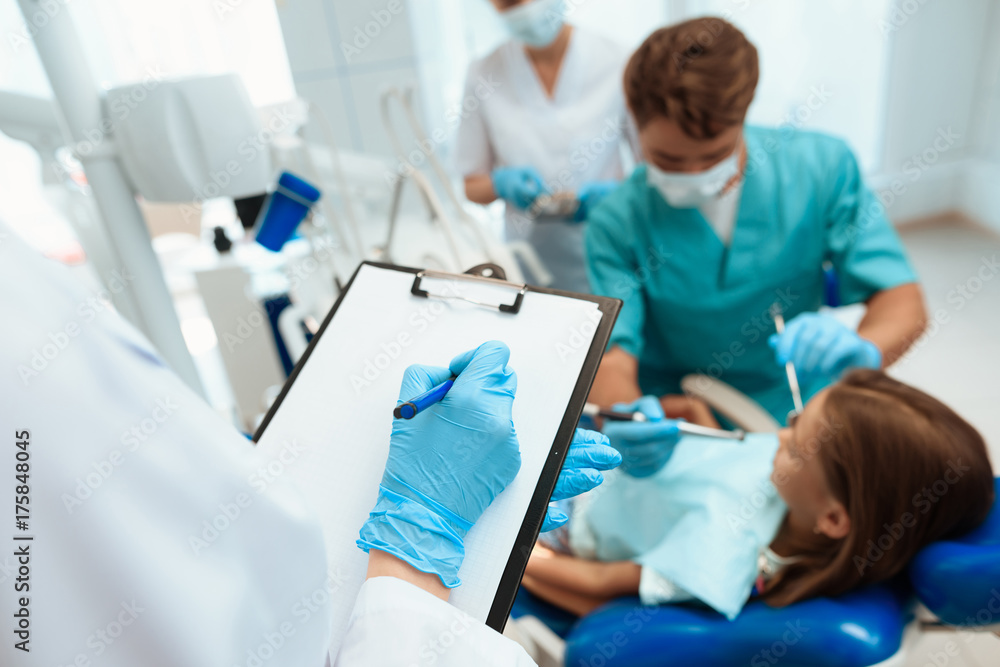 A nurse writes down the actions of a dentist in a medical journal while he is treating a girl A nurse writes down the actions of a dentist in a medical journal while he is treating a girl
