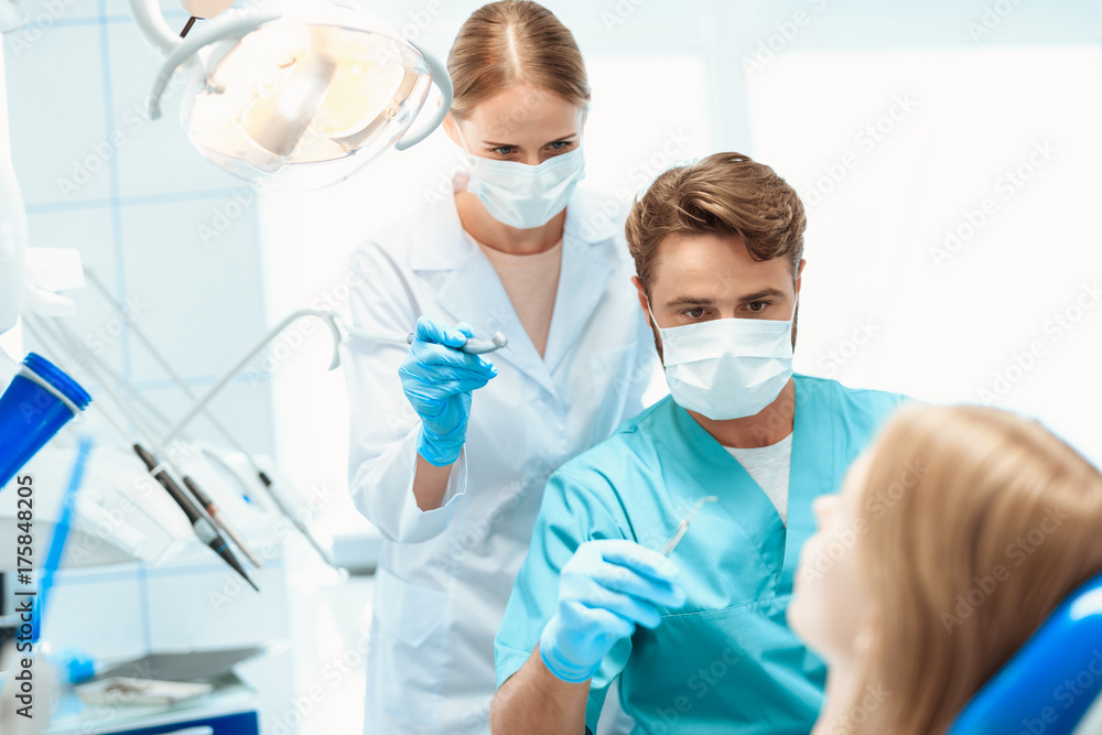 A dentist and a nurse treat a patient in a dental office. They put on medical masks A dentist and a nurse treat a patient in a dental office. They put on medical masks