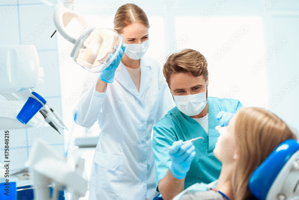 A dentist and a nurse treat a patient in a dental office. They put on medical masks A dentist and a nurse treat a patient in a dental office. They put on medical masks