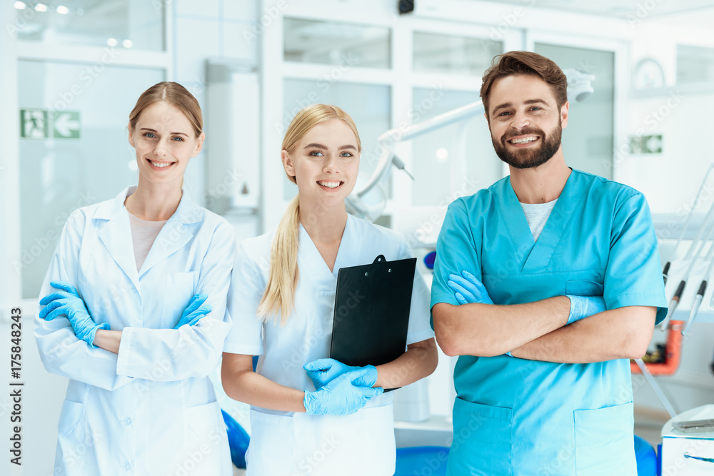 A dentist and two nurses are posing in a dental office. They are smiling A dentist and two nurses are posing in a dental office. They are smiling