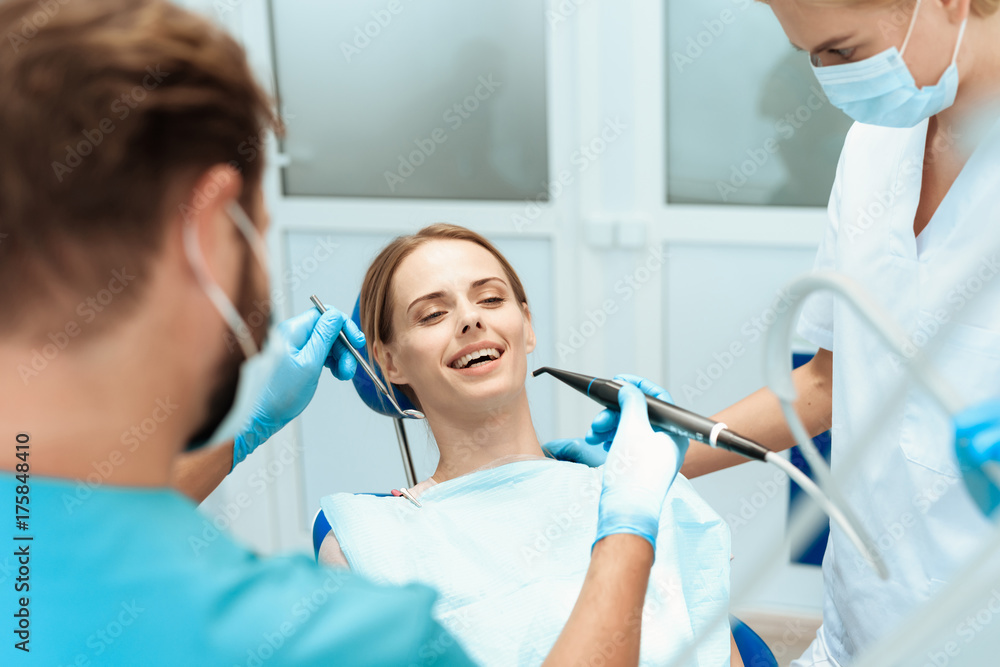 A woman is sitting in a dental chair, doctors dentists bent over her A woman is sitting in a dental chair, doctors dentists bent over her