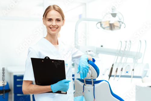 Female dentist posing against a background of dental equipment in a dental clinic. She hold tablet for papers