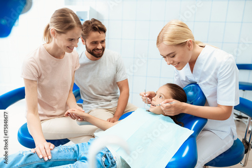 Parents brought their daughter to see a dentist. The girl is sitting in the dental chair. A doctor stands nearby © VadimGuzhva