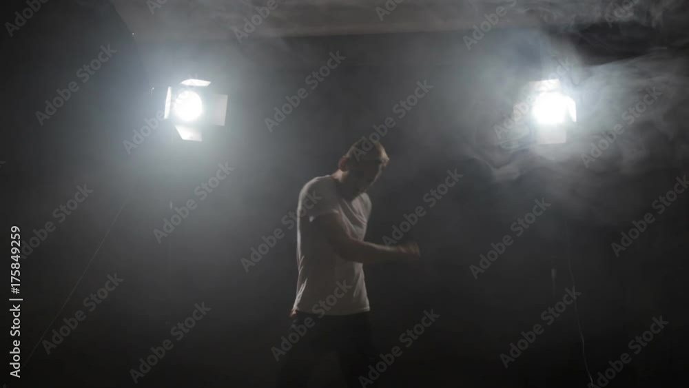 guy dancing in the dark in the backlight. a young man rhythmically moves his arms guy dancing in the dark in the backlight. a young man rhythmically moves his arms