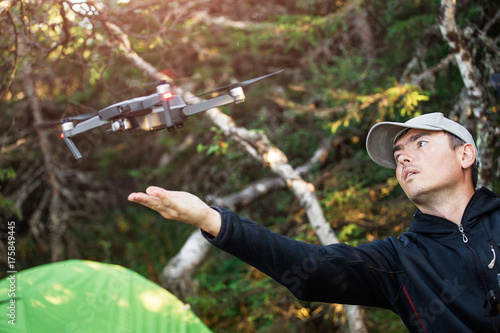 A man in a camping on the background of a tent launches a flying drone for taking photos and video
