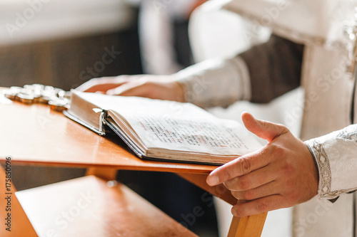 Priest hands close up on the opened bible book, during church service