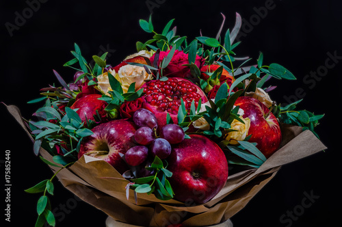 fresh autumn vegetarian fruity bouquet of apples, grapes, pomegranates and roses, with green leaves on a dark background