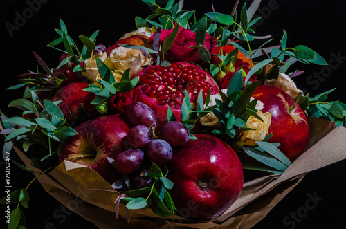 fresh autumn vegetarian fruity bouquet of apples, grapes, pomegranates and roses, with green leaves on a dark background