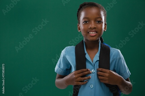 Fotografie School girl with backpack standing against chalk board