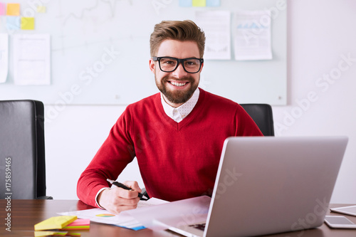 Businessman in office working with laptop and smiling at camera