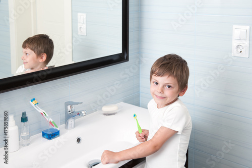 handsome smiling small boy with toothbrush in his hand standing in the bathroom