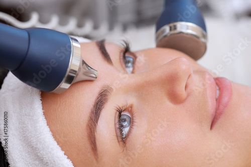 The cosmetologist makes the procedure an ultrasonic cleaning of the facial skin of a beautiful, young woman in a beauty salon.Cosmetology and professional skin care.