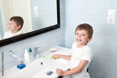 handsome healthy boy washing toothbrush over washbasin