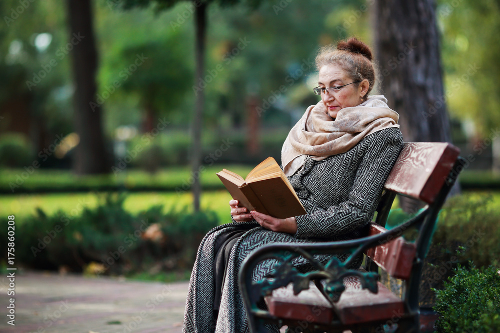 Счастливая старшая женщина, чтение книги в осеннем парке Счастливая старшая женщина, чтение книги в осеннем парке