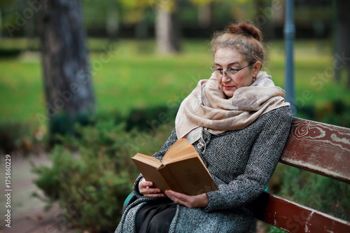 Счастливая старшая женщина, чтение книги в осеннем парке photo