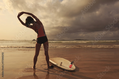 young woman surfer warming up on the beach