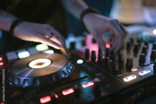 Hands of woman DJ tweak various track controls on dj's deck at night club 