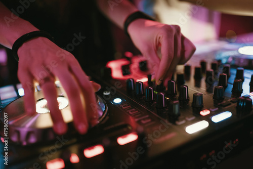 Obraz na plátně Hands of woman DJ tweak various track controls on dj's deck at night club