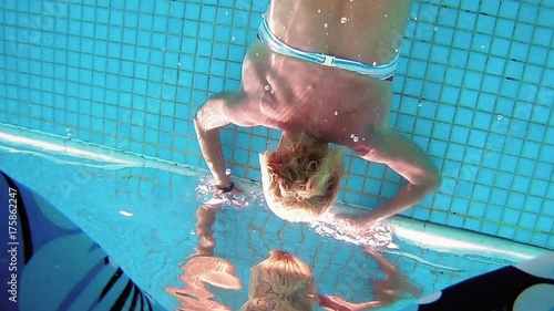 Beautiful woman is diving underwater in swimming pool and swims between her boyfriend legs. Fun and cute recreation shot of woman with a good figure.